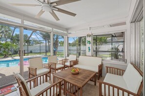 Ein Wintergarten mit Deckenventilator, großen Fenstern und Blick auf einen Pool.