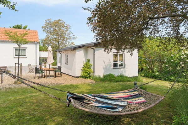 Une maison blanche avec un toit en tuiles, un hamac et une table avec des chaises dans la cour.