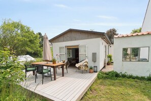 A wooden deck with outdoor furniture, a small building with an open door, and a garden area. - Holyday home in beatiful Vang (Hasle)