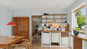 A kitchen with wooden cabinets, a dining table with chairs, a colorful backsplash, and a window with a view of greenery. - Holyday home in beatiful Vang (Hasle)