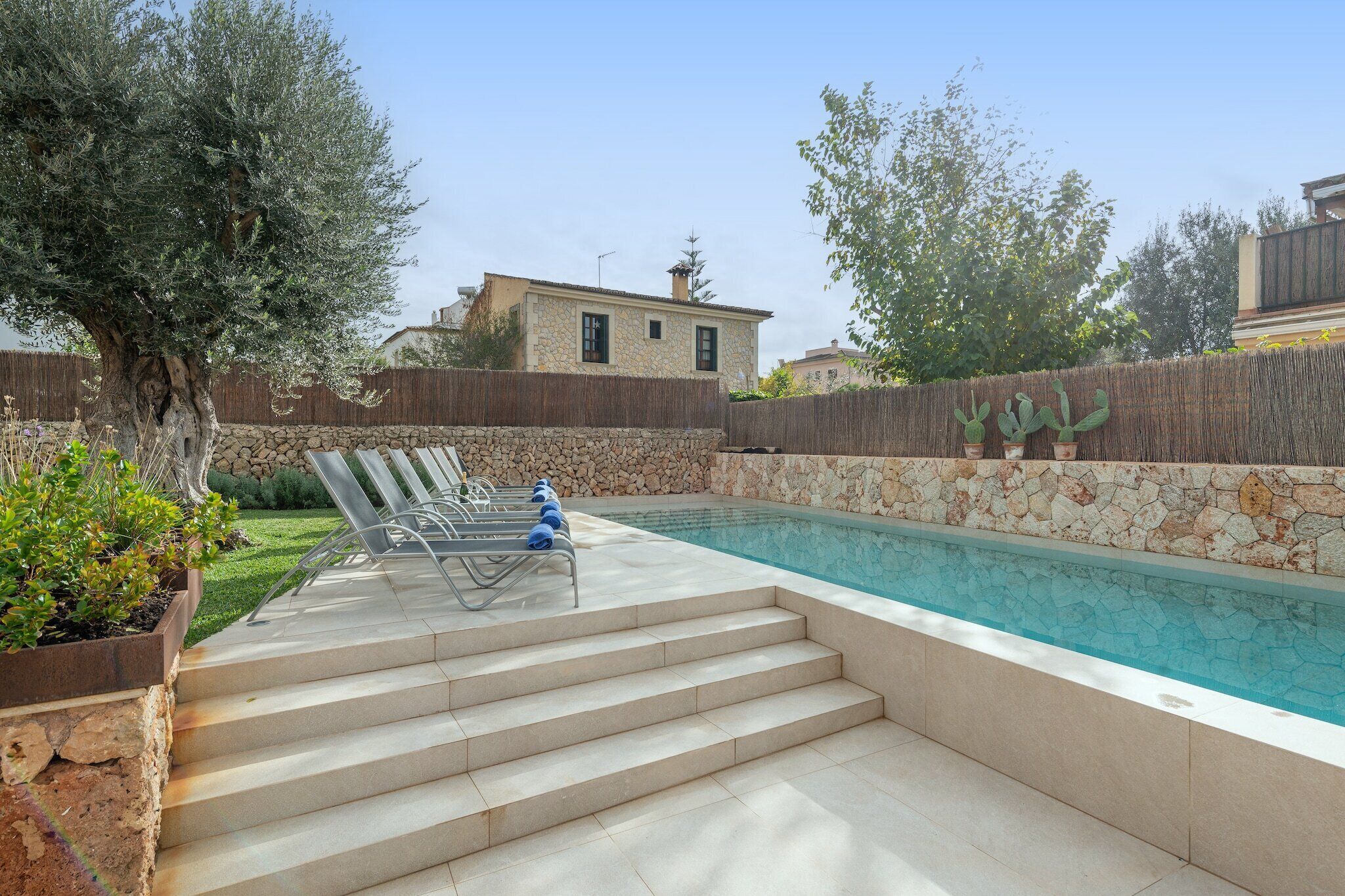 A swimming pool with steps leading up to it, surrounded by a stone wall and a wooden fence.