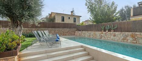 A swimming pool with steps leading up to it, surrounded by a stone wall and a wooden fence.