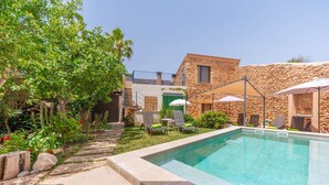 Ein Swimmingpool mit Liegestühlen und Sonnenschirmen, umgeben von einem Steinhaus und üppiger Vegetation.