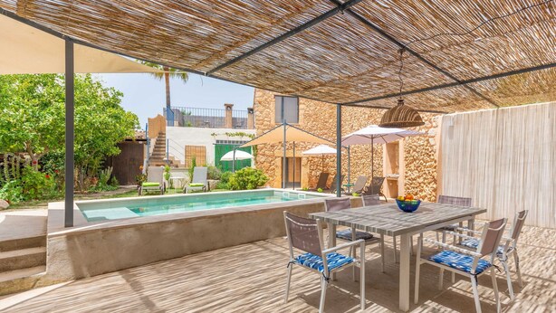 Eine Außenpatio mit Pool, überdachter Sitzgelegenheit und einem Steinhaus im Hintergrund.