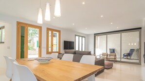 Ein modernes Wohnzimmer mit einem Holzesstisch, weißen Stühlen, einer Couch und einem Fernseher.