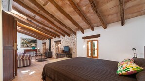 Ein Schlafzimmer mit einem großen Bett, Holzbalkendecke, Fernseher und einem Essbereich mit Tisch und Stühlen.