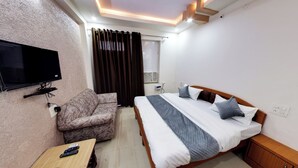 A hotel room with a bed, a sofa, a TV mounted on the wall, and a bedside table with a remote control. - Hotel Eleven Elites (Kota)