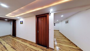 A hallway with wooden flooring, a wooden door with a security camera, and recessed lighting. - Hotel Eleven Elites (Kota)