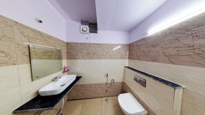 A bathroom with a white sink, mirror, and toilet, marble walls, and a shower area. - Hotel Eleven Elites (Kota)