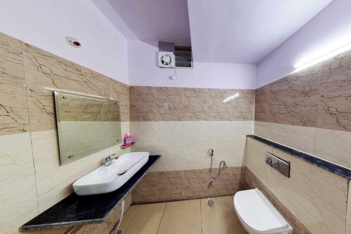 A bathroom with a white sink, mirror, and toilet, marble walls, and a shower area.