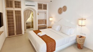 Ein Hotelzimmer mit einem großen Bett, einem Schminktisch mit Spiegel, einer Klimaanlage und einer kleinen Sitzecke mit einer Bank.
