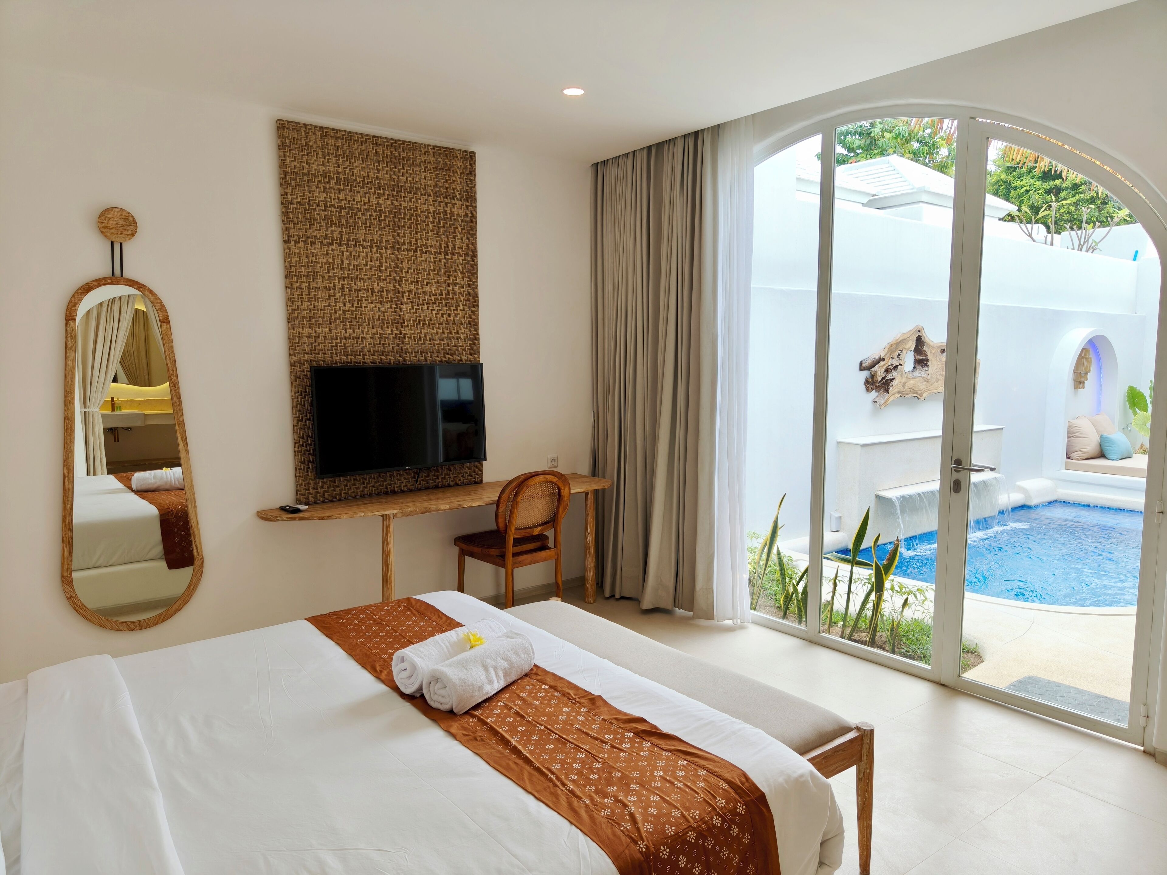 Habitación de hotel con cama, televisión, escritorio, silla y vista a una piscina.