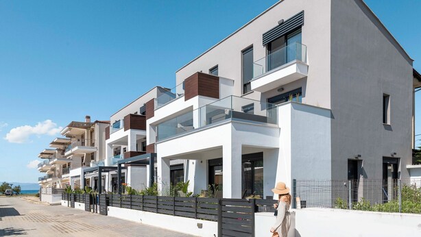 Un moderno edificio residencial con varios balcones, un sendero pavimentado y una vista despejada al mar.