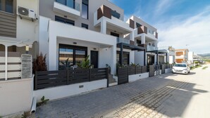 Un edificio residencial moderno con camino de entrada pavimentado, varios balcones y un coche estacionado al frente.