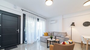 Una sala de estar moderna con un sofá, una mesa de centro y una silla. Hay una puerta, una ventana con cortinas y un reloj en la pared.