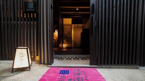 A hotel entrance with a wooden facade, a pink carpet with Japanese characters, and a signboard with Japanese text. - Oyado Kinokuniya Kagomachi (Nagasaki)
