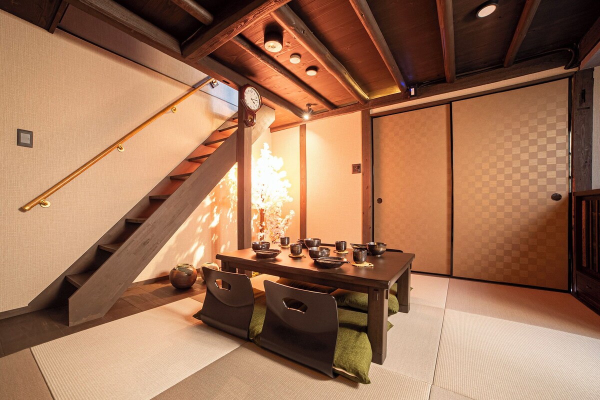 A traditional Japanese room with tatami flooring, a low table set with tea utensils, a clock on the wall, and a sliding door.