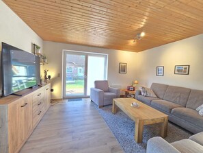 A modern living room with a flat-screen TV, a sofa, a chair, a coffee table, and a wooden ceiling. - Vacation home Deichkrone - Comfortable vacation home Deichkrone with garden and (Dornum)