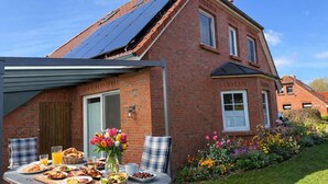 A brick house with a solar panel roof, a dining table with breakfast, and a garden with flowers.