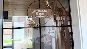 A wooden sign with coordinates above a glass door with a welcome message.