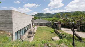 Een modern gebouw met een grote glazen gevel, een patio met buitenmeubilair en uitzicht op een bergachtig landschap.