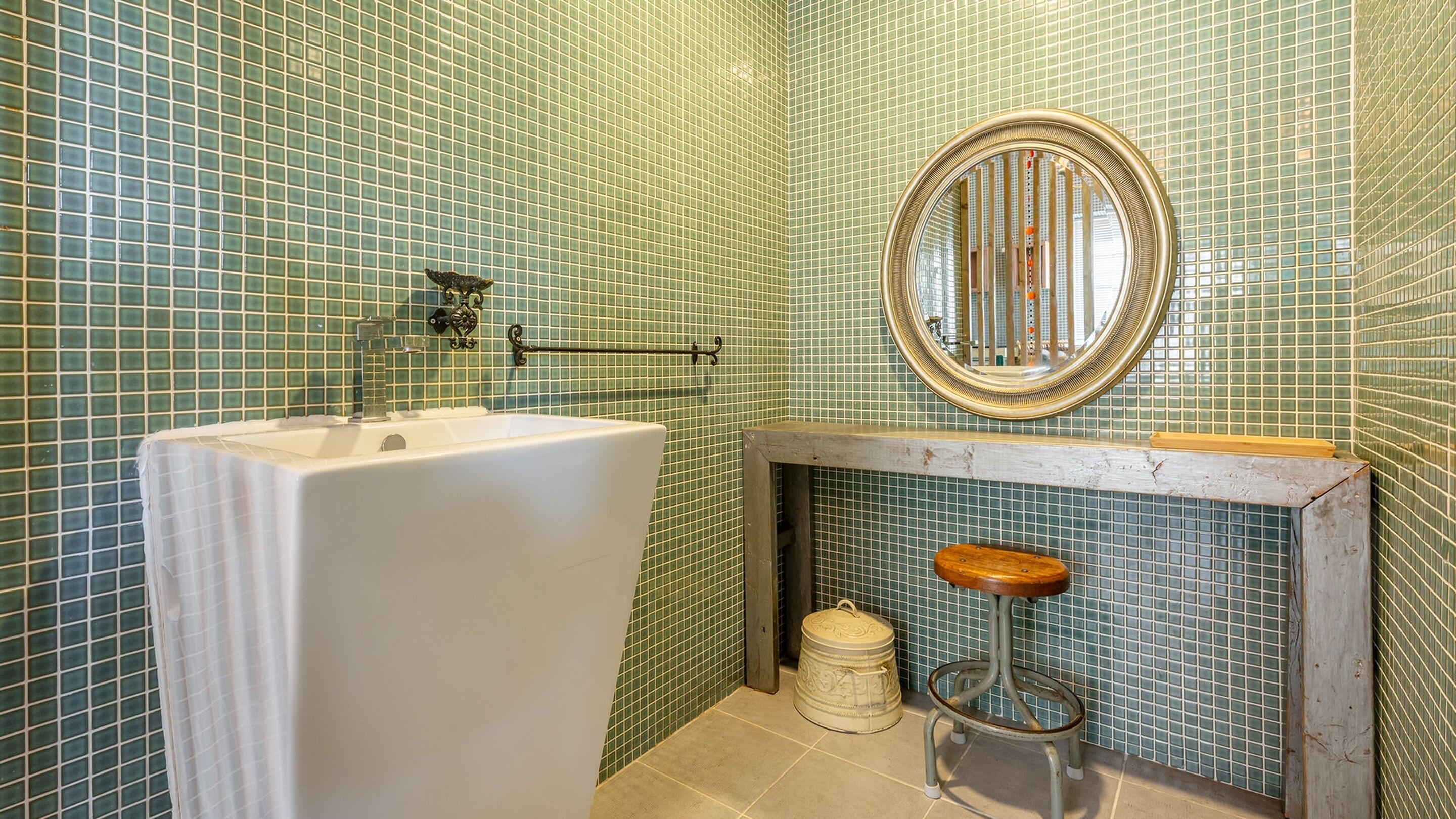 A bathroom with a bathtub, a wooden stool, a mirror, and a tiled wall.