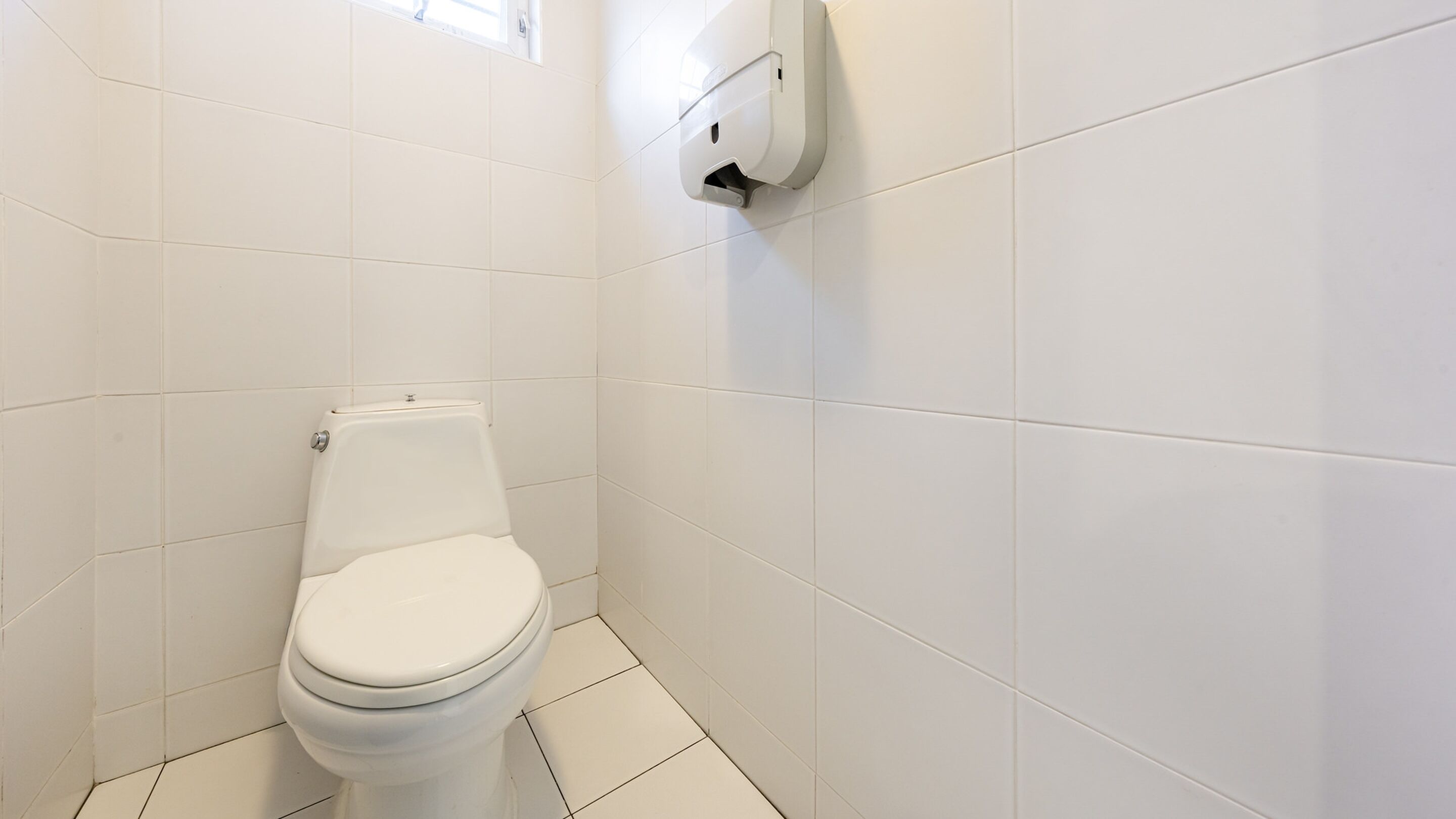 A small, white-tiled bathroom with a toilet and a wall-mounted hand dryer.