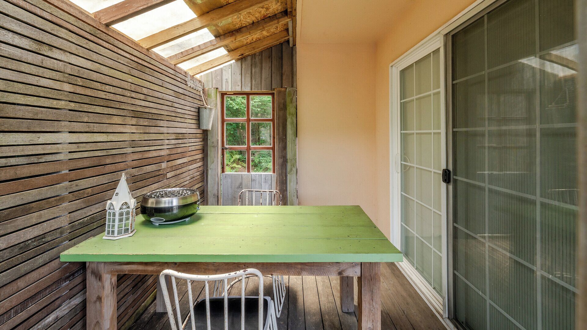 A wooden deck with a green table, a metal bowl, and a white chair.