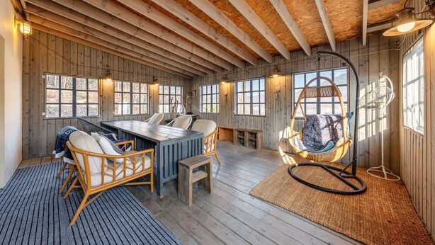 Een houten interieur met een eettafel, stoelen, een hangstoel en grote ramen.