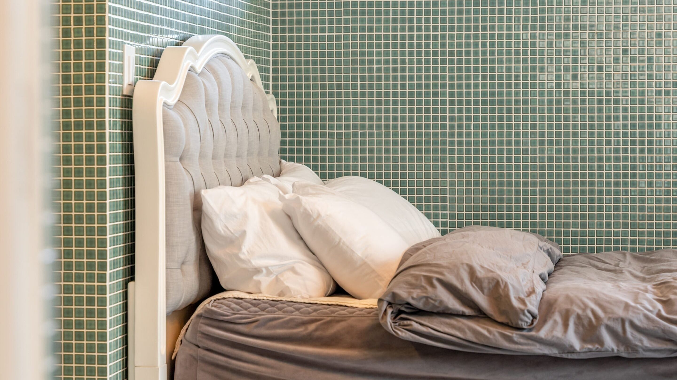 A bed with a headboard, pillows, and a blanket in a room with green tiled walls.
