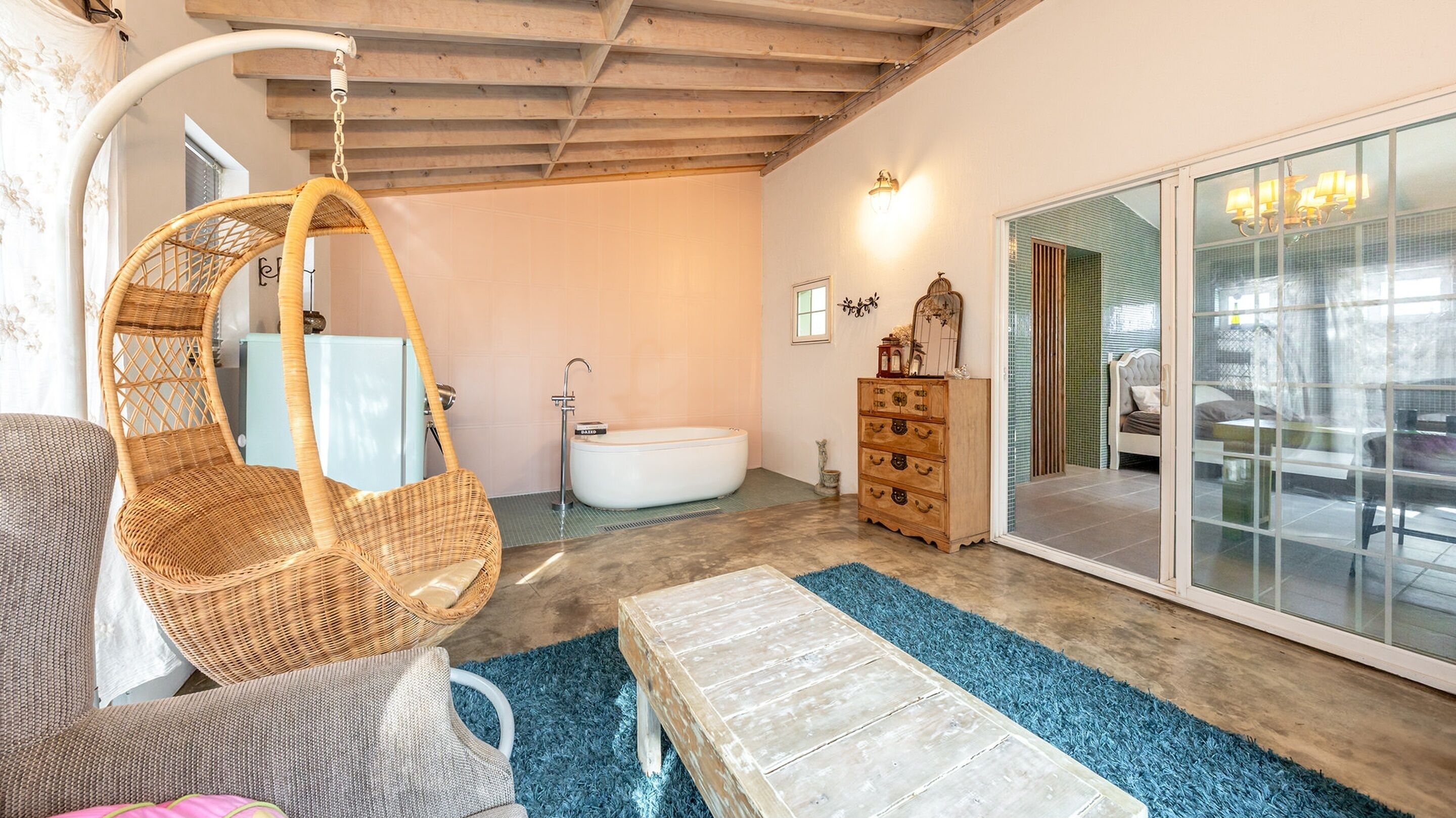 A room with a hanging chair, a bathtub, a dresser, and a large mirror.