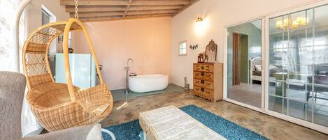 A room with a hanging chair, a bathtub, a dresser, and a large mirror.