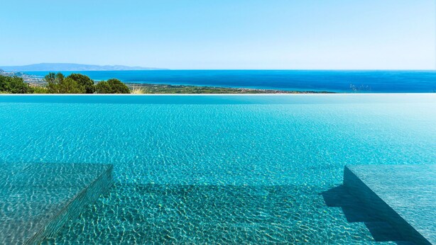 Ein klarer Blick auf einen Infinity-Pool vor einer Küstenlandschaft und entfernten Bergen.