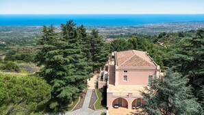 Eine mediterrane Villa mit Terrakotta-Dach, umgeben von üppiger Vegetation mit Blick auf eine Küstenlandschaft.