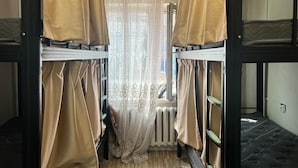 Een slaapkamer met stapelbedden, gordijnen, een radiator en een raam met kantgordijnen.