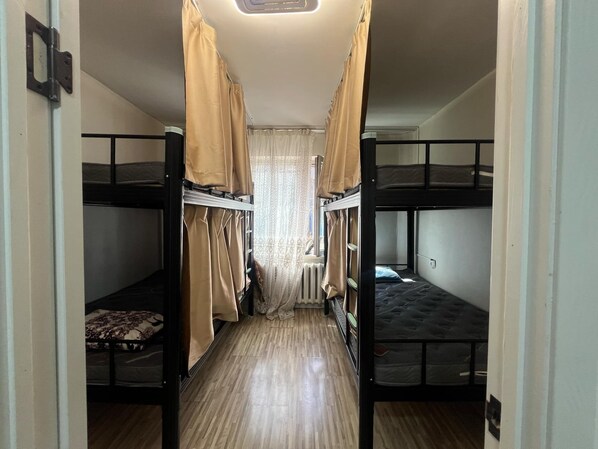 Un pasillo estrecho con literas a ambos lados, un radiador y una ventana con cortinas.