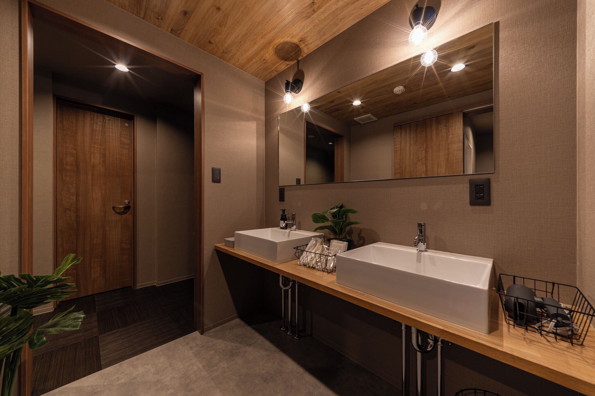 Un baño moderno con dos lavamanos, un espejo grande y detalles de techo de madera.