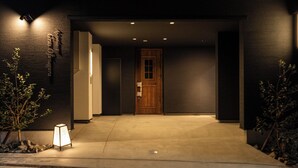 A modern building entrance with a dark facade, a wooden door, and a well-lit pathway. - Oyado Kinokuniya Takaramachi (Nagasaki)