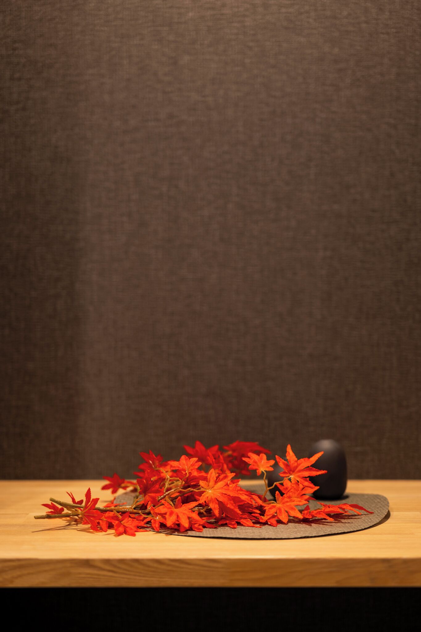 Een houten tafel met een zwarte vaas en rode bloemen.