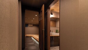 A hallway with a wooden shoe rack holding black slippers, leading to a room with a wooden ceiling and a visible sink. - Oyado Kinokuniya Takaramachi (Nagasaki)
