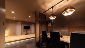 A modern dining area with a wooden table and chairs, recessed ceiling lights, and a decorative hanging light fixture. - Oyado Kinokuniya Takaramachi (Nagasaki)