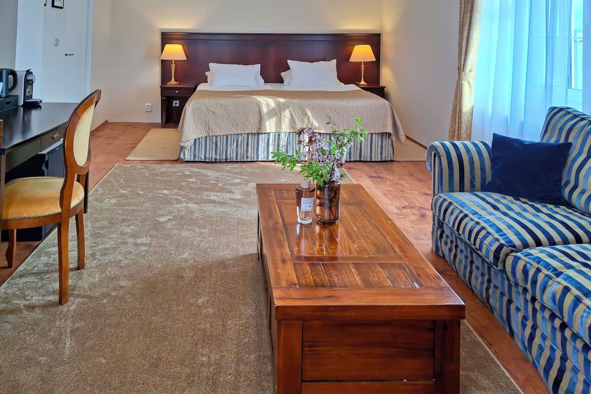 Una habitación de hotel con cama, sofá, una mesita de madera, una silla y un escritorio.