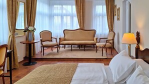 A hotel room with a bed, two armchairs, a sofa, a small table with a vase, and a lamp.