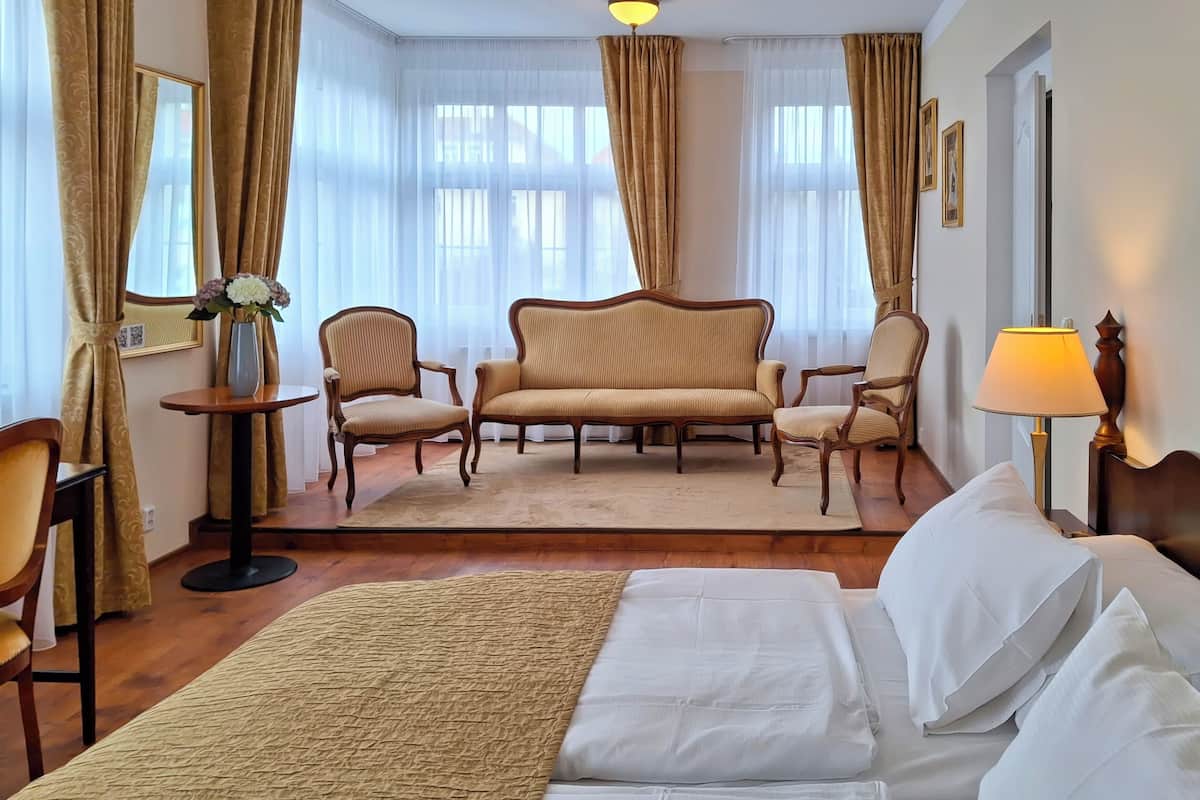 Habitación de hotel con una cama, dos sillones, un sofá, una mesita con un florero y una lámpara.
