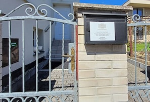 Une entrée fermée par un portail, agrémentée d’une plaque et d’une boîte aux lettres.
