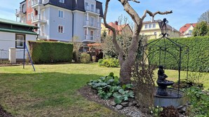 A residential area with a well-maintained lawn, a garden with a birdbath, and a row of houses with balconies.