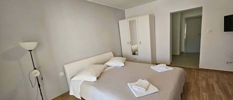 A bedroom with a bed, a wardrobe, a floor lamp, and a television.