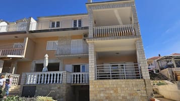 Un edifici residencial de diverses plantes amb balcons, una petita zona de jardí i un cel blau clar.