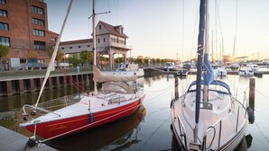 Un puerto deportivo con barcos amarrados, un edificio con balcón y una masa de agua tranquila.