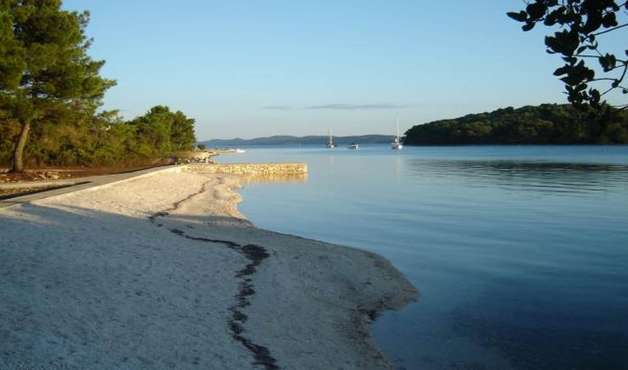 A beach with a sandy shore, calm water, and a few sailboats in the distance.